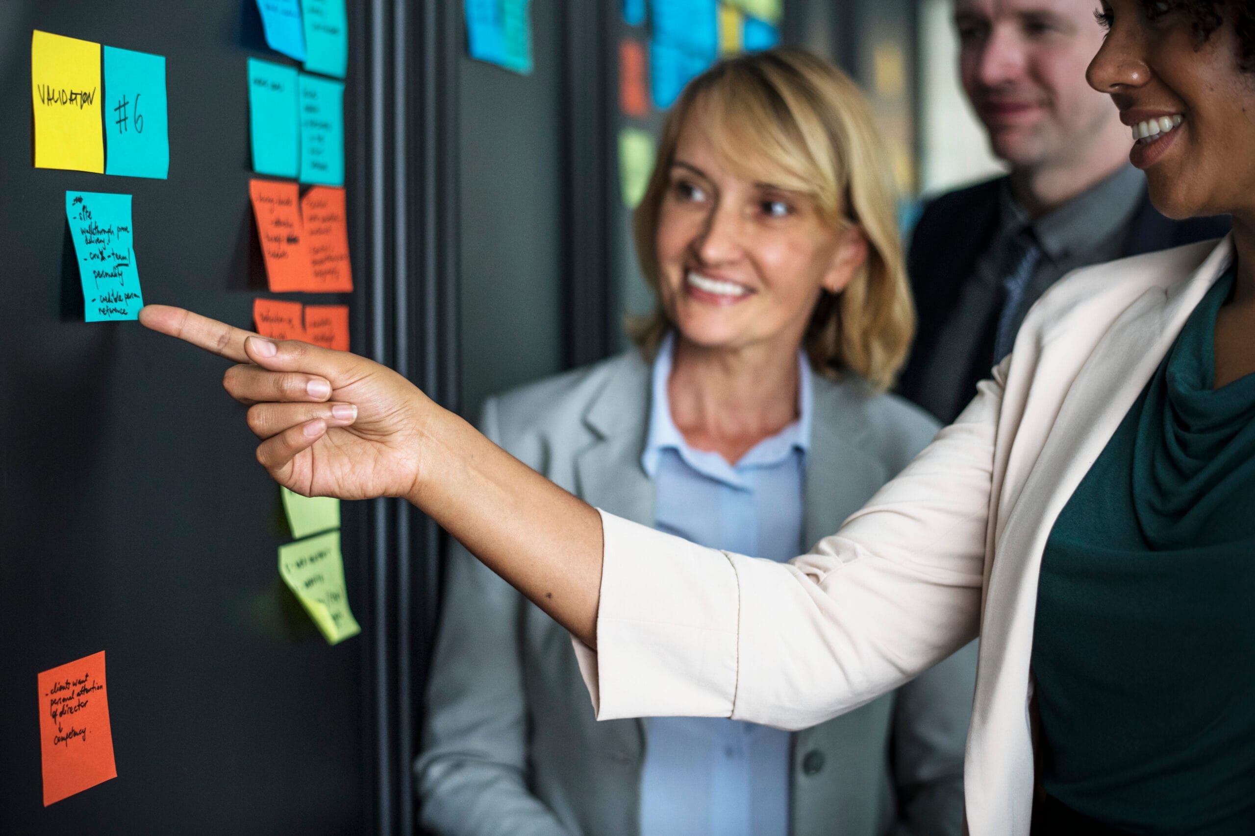 Business people planning tasks with sticky notes Three business people are gathered around several sticky notes.